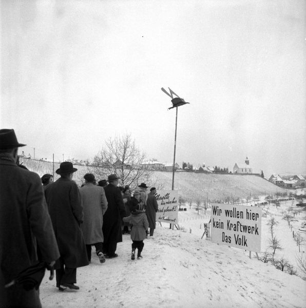 Das Bild stammt aus den 1950er Jahren und zeigt eine Menschenkette sowie Protestplakate entlang des Rheinufers bei Rheinau. Anlass des Protests ist der geplante Bau eines Wasserkraftwerks im Rhein bei Rheinau. 